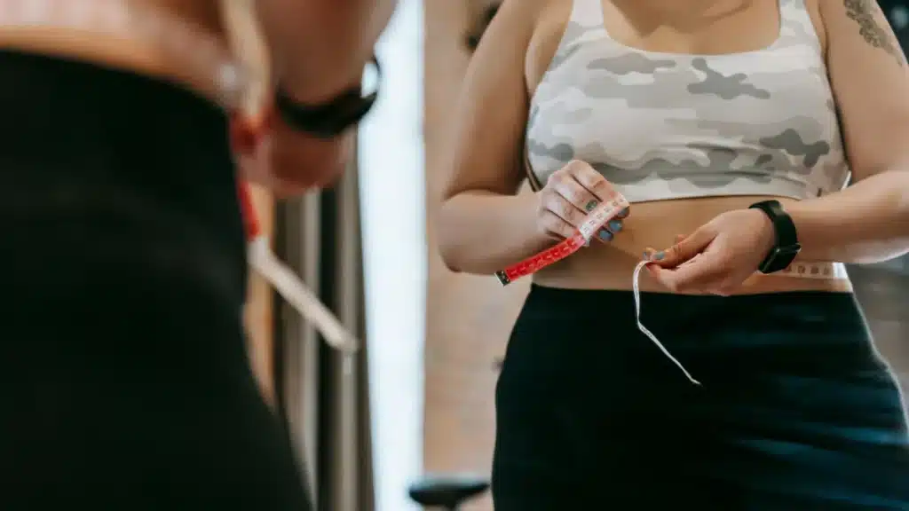 Woman measuring flat belly waist with tape in gym